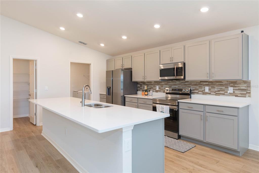 A kitchen features gray cabinets, white countertops, a center island, and a tiled backsplash — 35171 CRESCENT CREEK DRIVE, ZEPHYRHILLS, FL