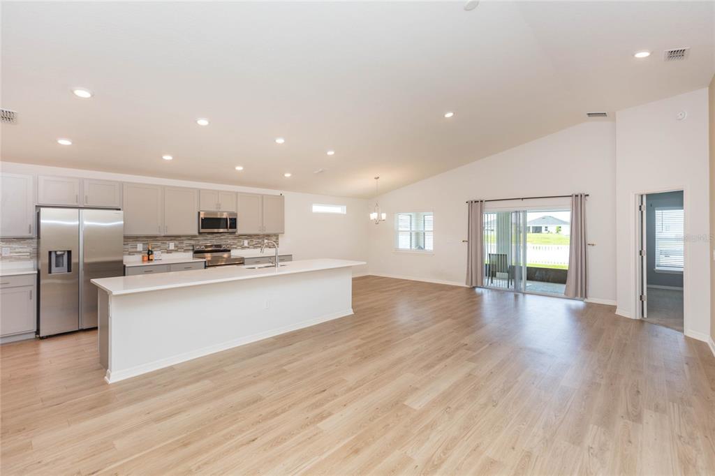 A bright, open-concept kitchen and living area featuring light wood floors and white cabinetry — 35171 CRESCENT CREEK DRIVE, ZEPHYRHILLS, FL