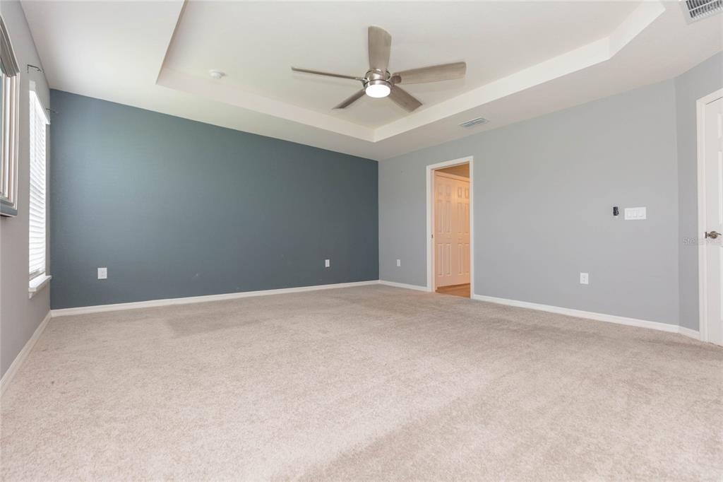 A bedroom with a tray ceiling, ceiling fan, blue accent wall, and beige carpet — 35171 CRESCENT CREEK DRIVE, ZEPHYRHILLS, FL