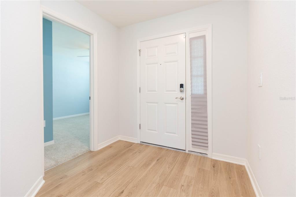 An entryway features light wood-look flooring, a white front door with a sidelight, and a doorway — 35171 CRESCENT CREEK DRIVE, ZEPHYRHILLS, FL