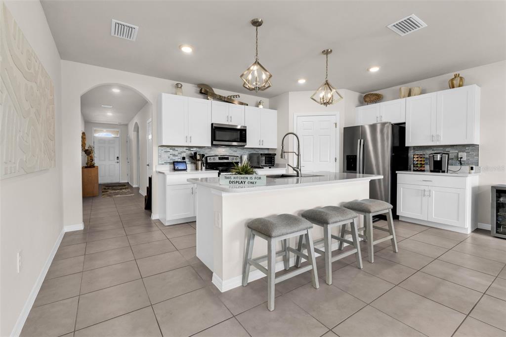 A modern kitchen features white cabinetry, a central island with three stools, and tile flooring — 4195 MANATEE LANE, PUNTA GORDA, FL