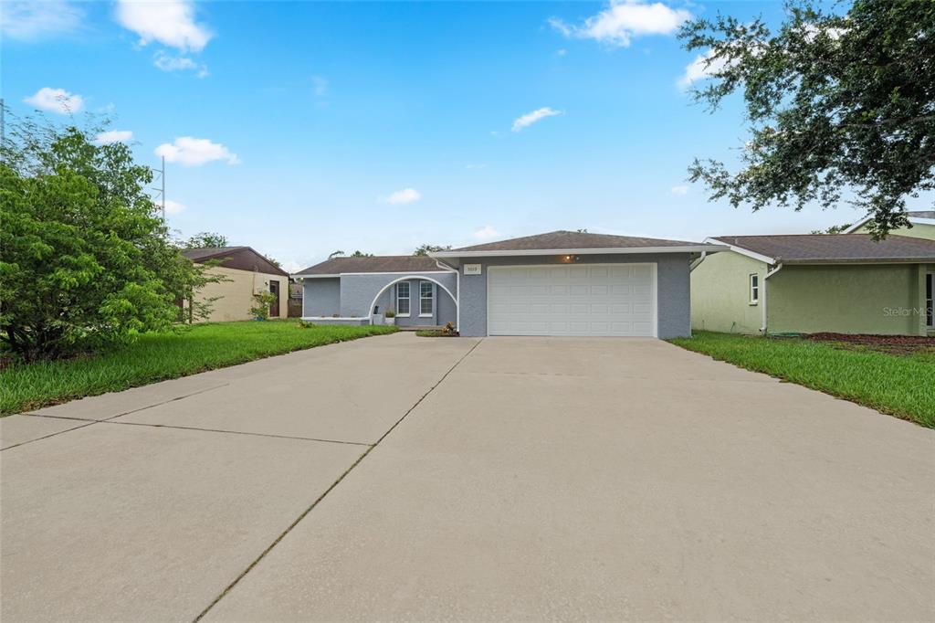 A single-story house with a gray exterior, a white garage door, and a concrete driveway — 5019 LARCH LANE, NEW PORT RICHEY, FL