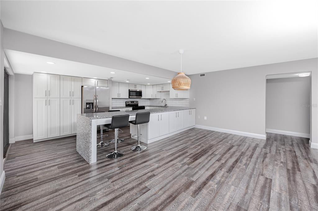 A modern kitchen features white cabinetry, granite countertops, a breakfast bar, and wood-look flooring — 7510 SUNSHINE SKYWAY LANE S UNIT P4, ST PETERSBURG, FL