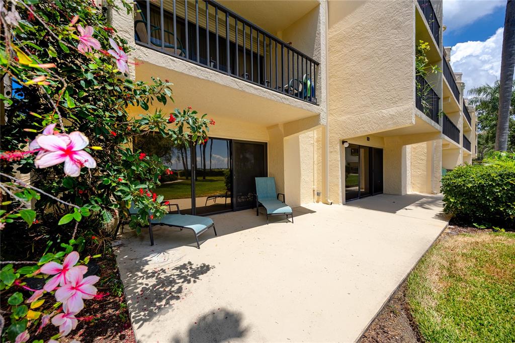 A ground-floor patio with two lounge chairs sits outside a building with sliding glass doors — 7510 SUNSHINE SKYWAY LANE S UNIT P4, ST PETERSBURG, FL