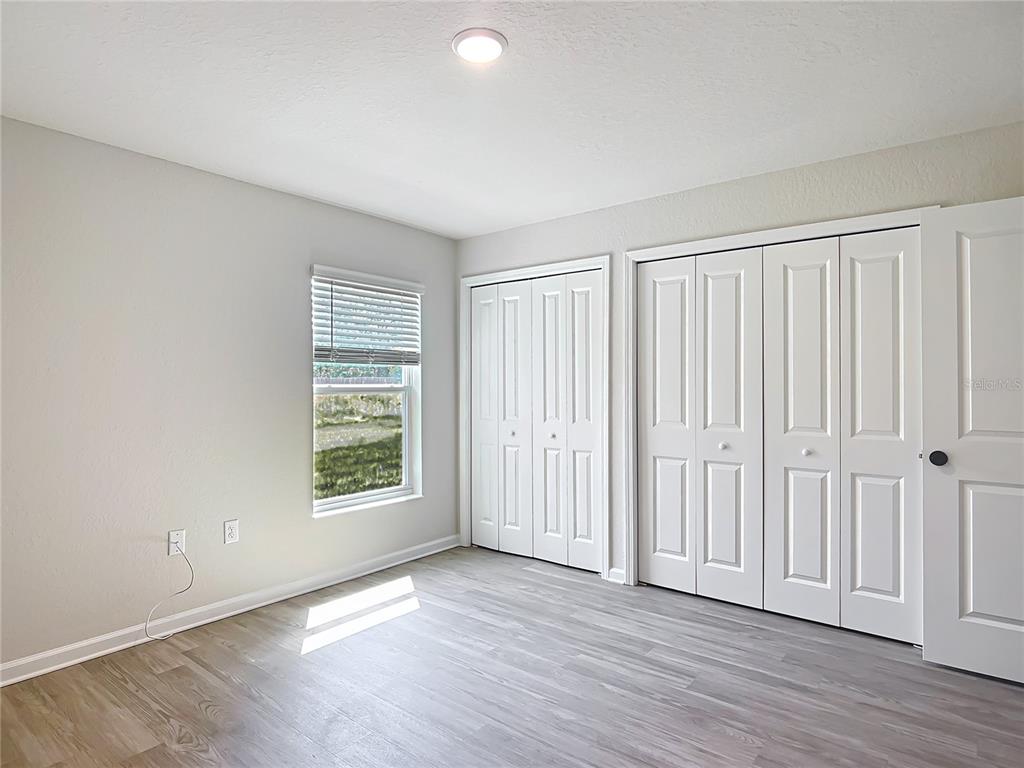 A bedroom features light gray walls, wood-look flooring, a window, and white closet doors — 6040 W OAK PARK BOULEVARD, HOMOSASSA, FL