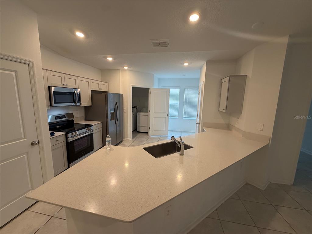 A kitchen features white cabinets, stainless steel appliances, a quartz island, and tile flooring — 314 LAWSON AVENUE, HAINES CITY, FL