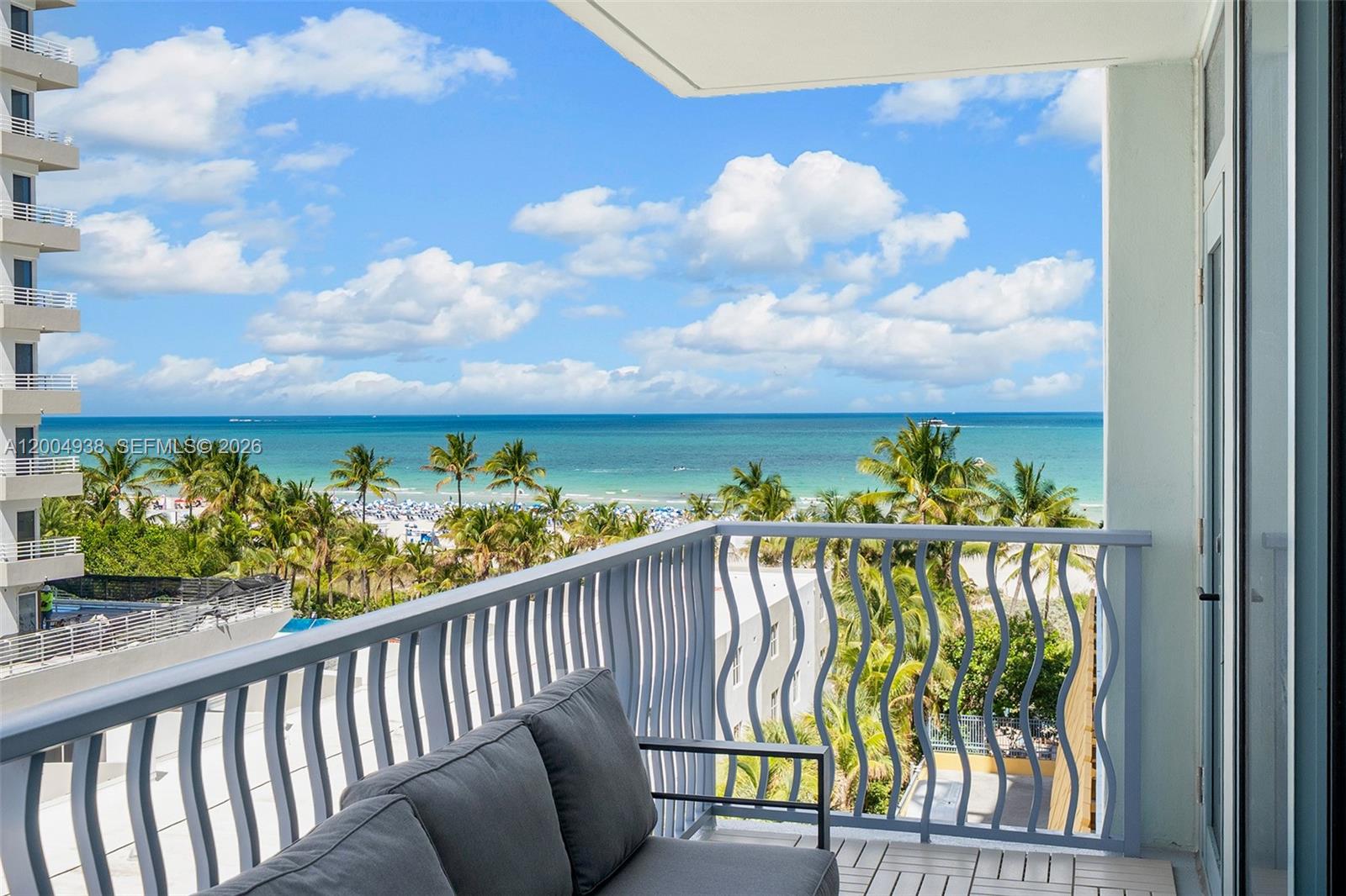 A balcony with a grey sofa overlooks a beach, palm trees, and the ocean — 1500 Ocean Dr # 607, Miami Beach FL 33139, MIAMI BEACH, FL