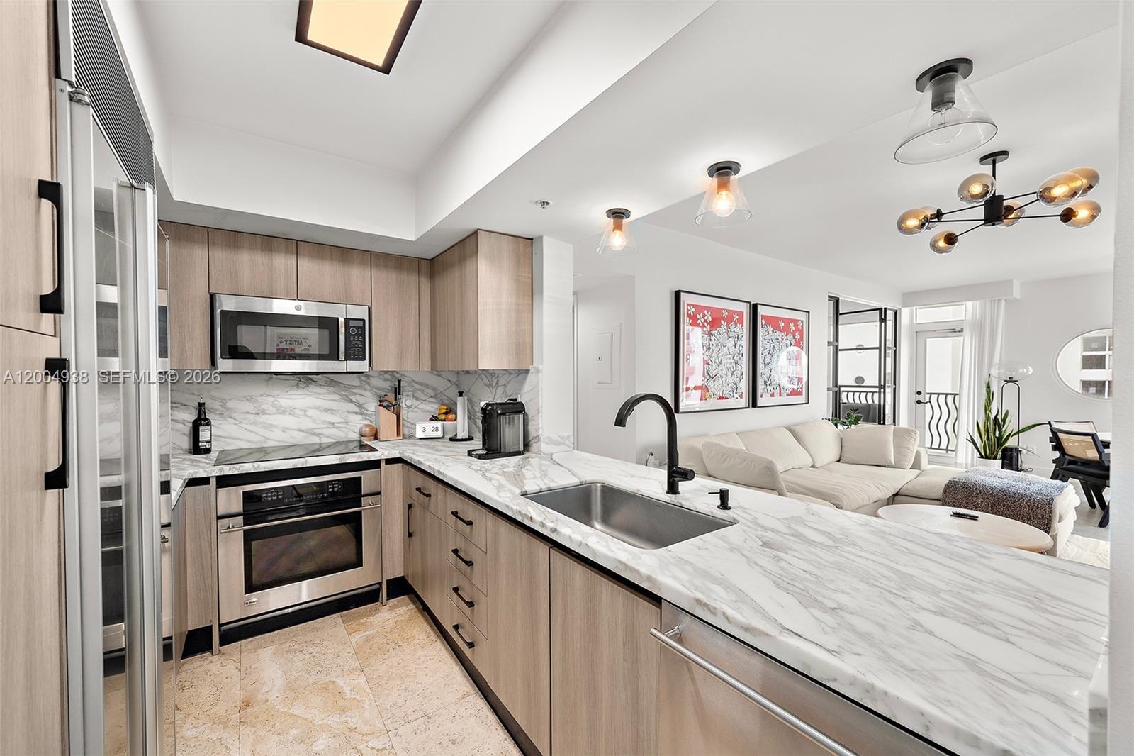 A modern kitchen features light wood cabinets, marble countertops, and stainless steel appliances — 1500 Ocean Dr # 607, Miami Beach FL 33139, MIAMI BEACH, FL