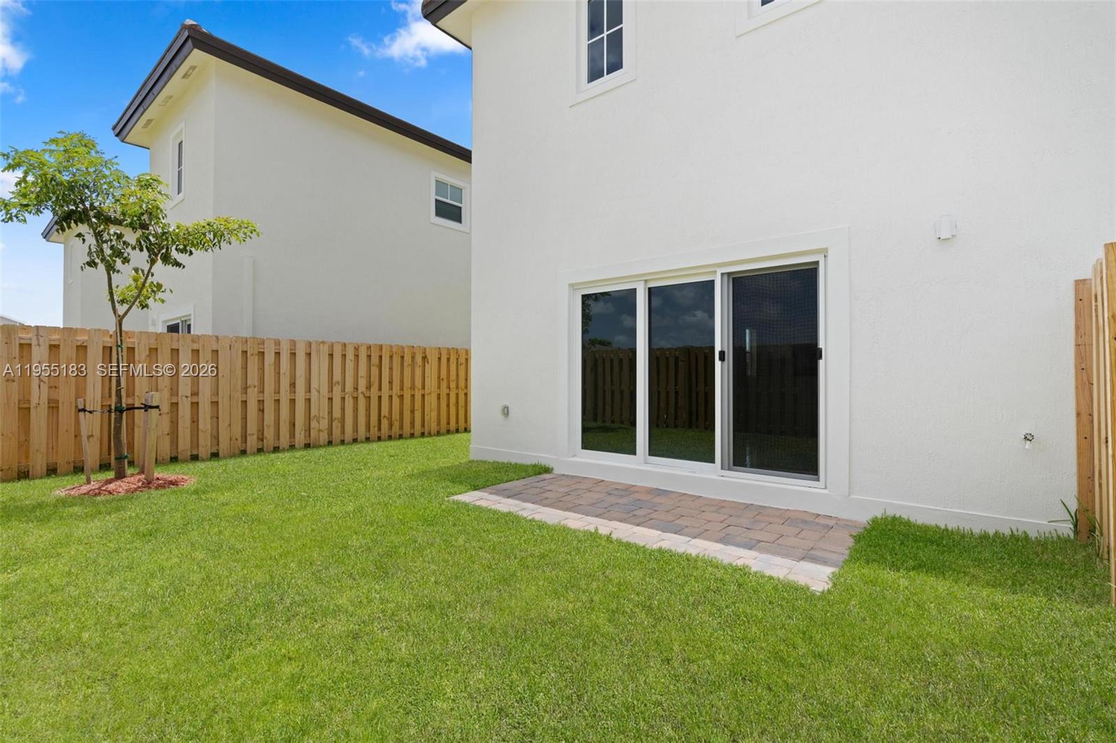 A white house exterior features a small paver patio and a sliding glass door — 27333 SW 133rd Path, Homestead FL 33032, HOMESTEAD, FL