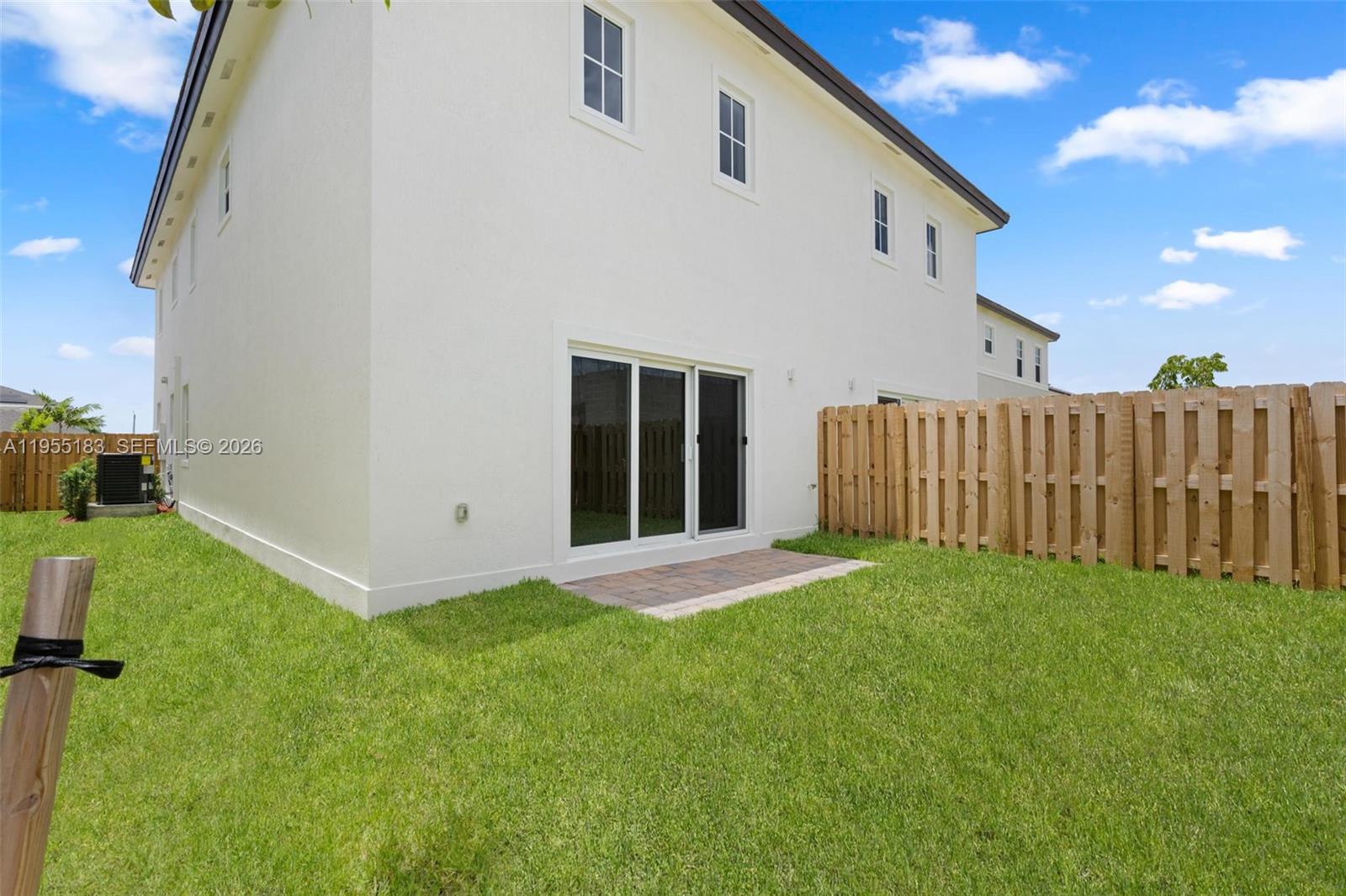 The exterior of a two-story white house features a small patio and a wooden fence — 27333 SW 133rd Path, Homestead FL 33032, HOMESTEAD, FL