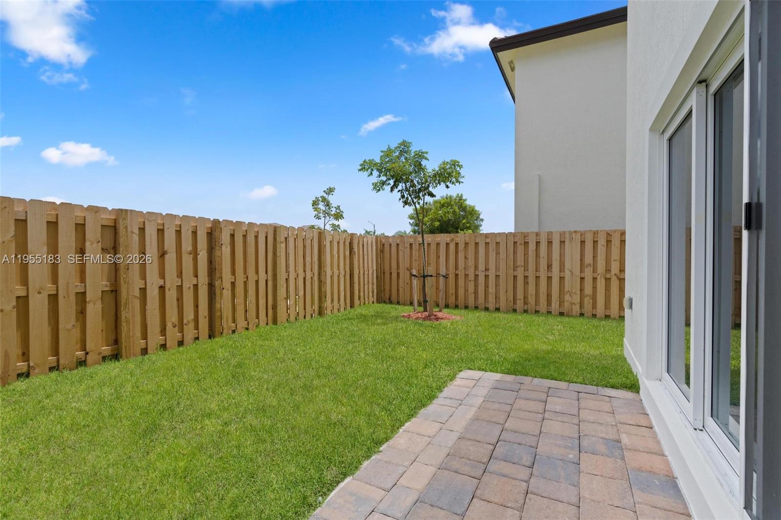 A backyard features a small paved patio, a grassy lawn, and a wooden privacy fence — 27333 SW 133rd Path, Homestead FL 33032, HOMESTEAD, FL