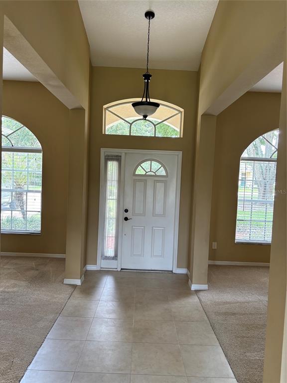 An entryway features a tiled floor, beige walls, arched windows, and a central pendant light — 561 STRATHCLYDE COURT, APOPKA, FL
