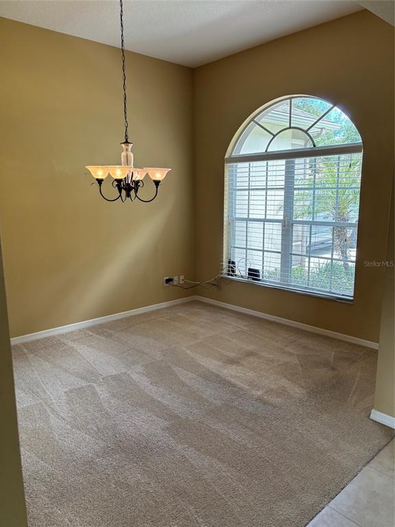 An empty room with tan walls, carpeted flooring, a chandelier, and an arched window — 561 STRATHCLYDE COURT, APOPKA, FL