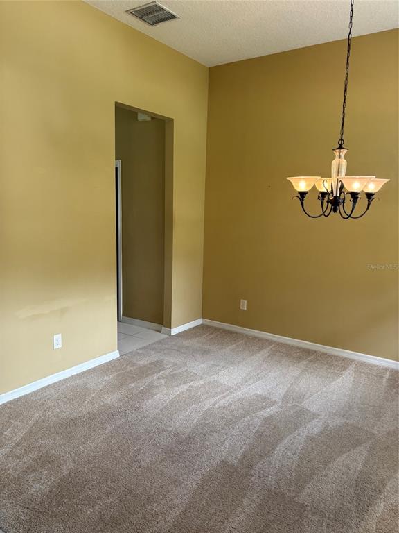 A dining room features tan walls, beige carpeting, and a hanging chandelier — 561 STRATHCLYDE COURT, APOPKA, FL
