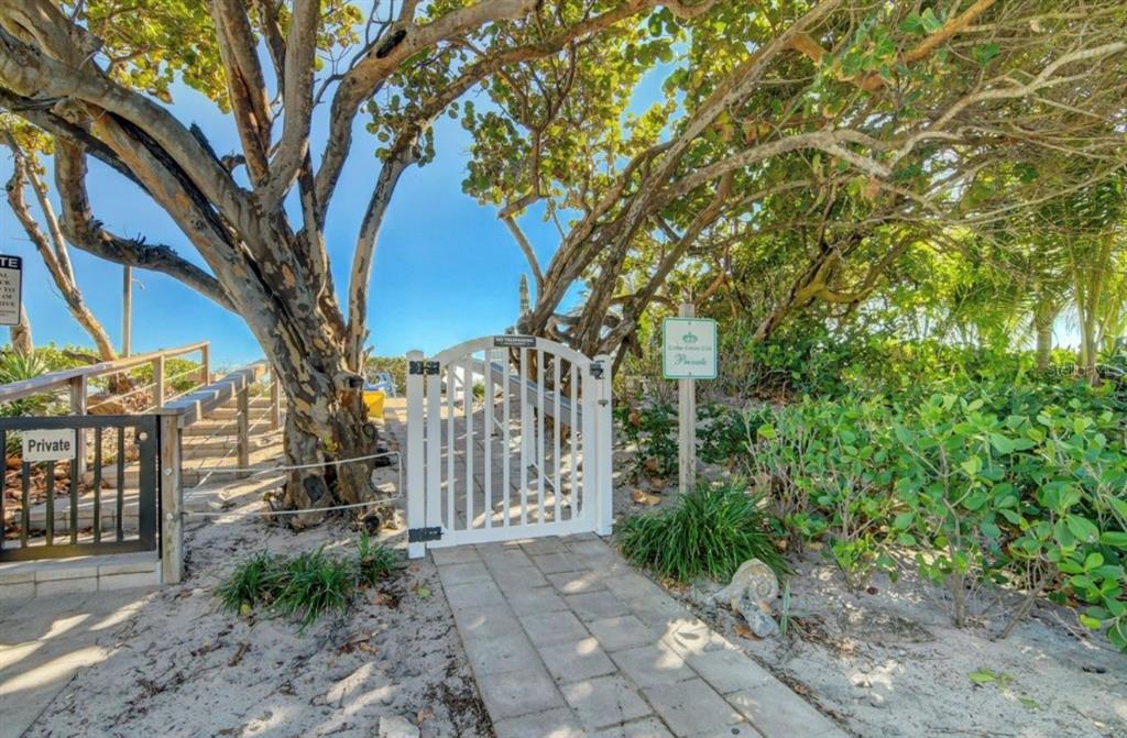 A white gate leads to a sandy beach path surrounded by trees and lush vegetation — 5540 N OCEAN BOULEVARD UNIT 206, OCEAN RIDGE, FL