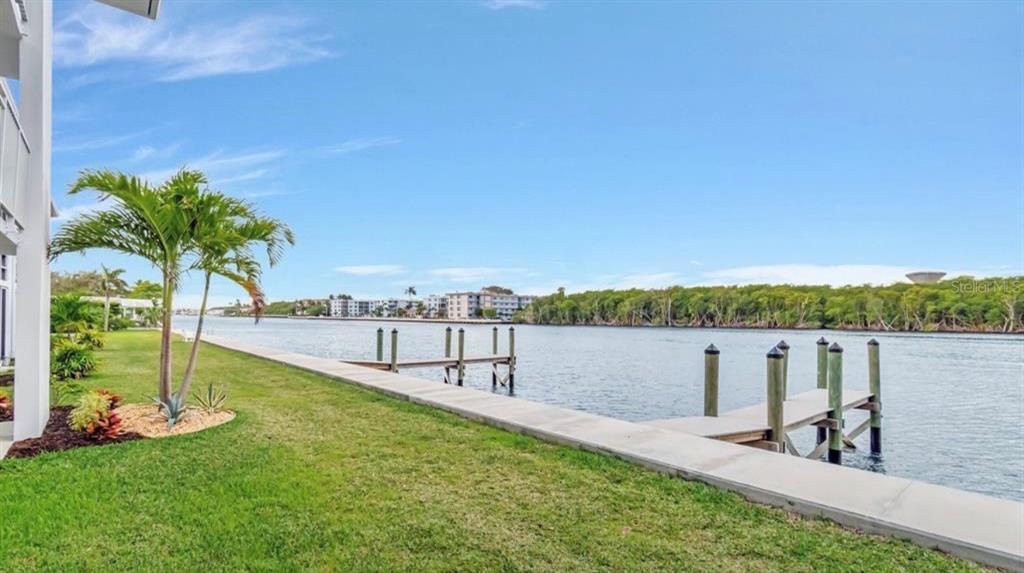 A concrete walkway runs along a grassy lawn beside a canal with a wooden dock — 5540 N OCEAN BOULEVARD UNIT 206, OCEAN RIDGE, FL