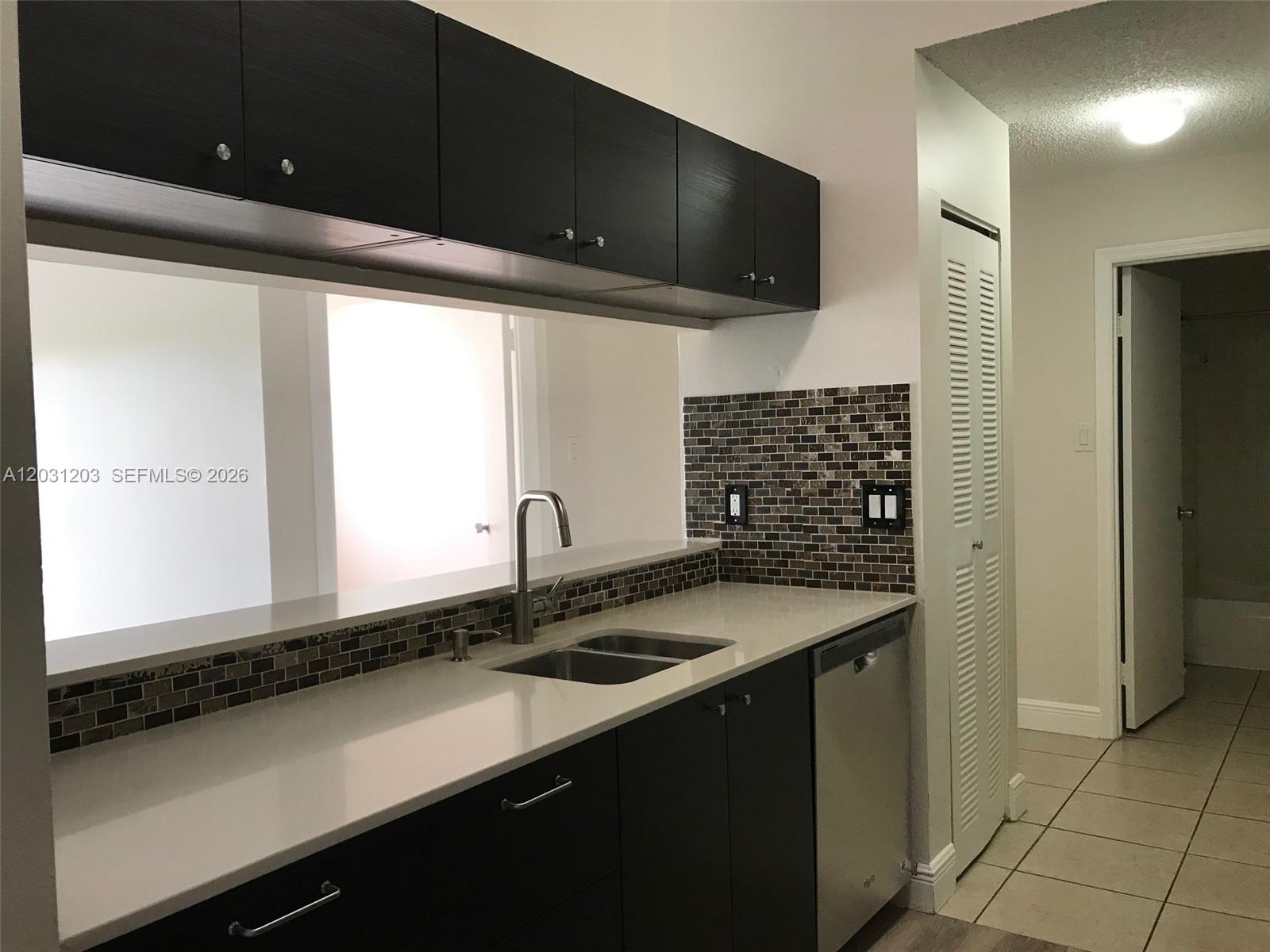 A kitchen features dark cabinets, white countertops, a stainless steel sink, and a tiled backsplash — 15780 SW 106th Ter # 306, Miami FL 33196, MIAMI, FL