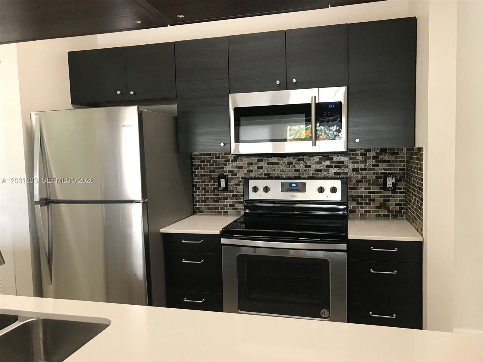 A kitchen features dark wood cabinets, stainless steel appliances, and a mosaic tile backsplash — 15780 SW 106th Ter # 306, Miami FL 33196, MIAMI, FL