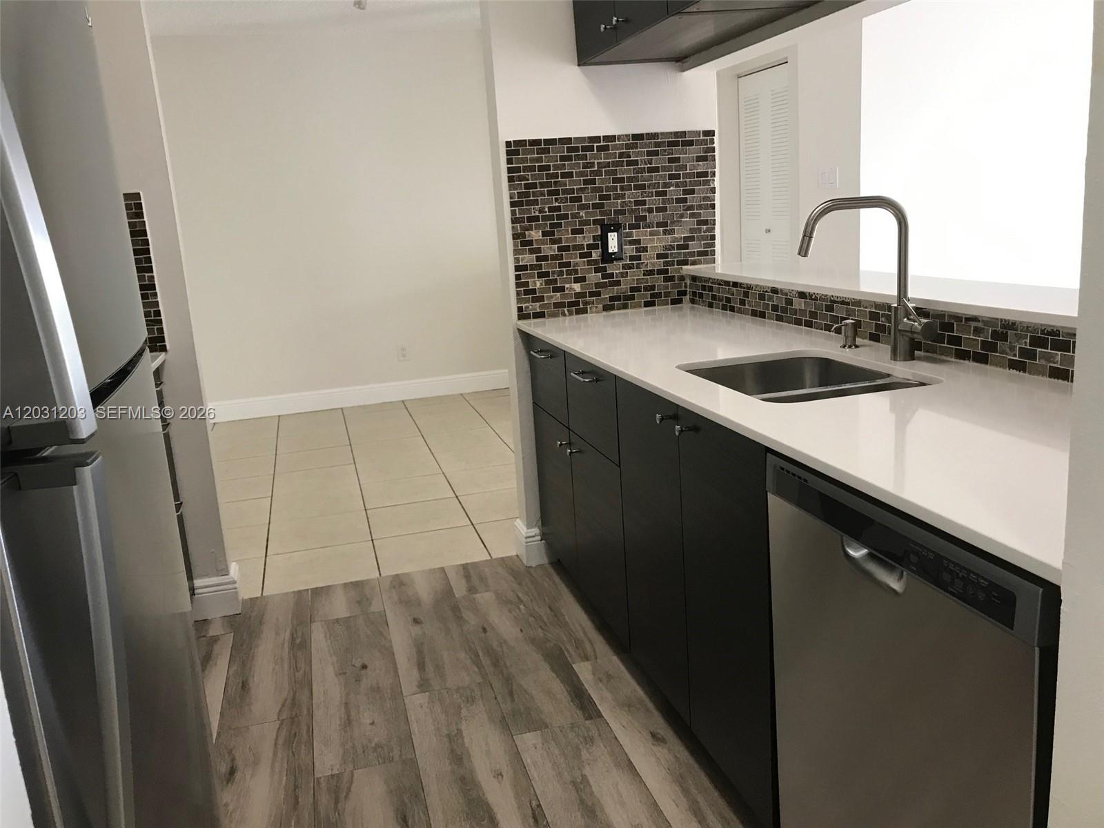 A kitchen features dark cabinets, white countertops, a stainless steel dishwasher, and a tiled backsplash — 15780 SW 106th Ter # 306, Miami FL 33196, MIAMI, FL