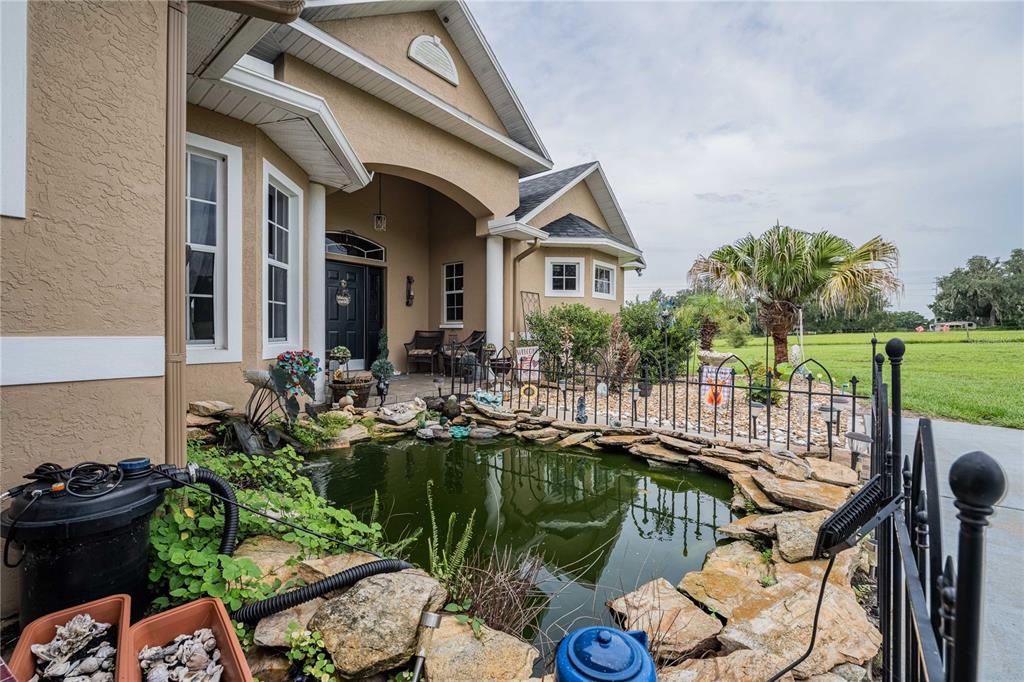 A house exterior features a stone-lined pond in the foreground and a covered entryway — 4280 TURNER ROAD, MULBERRY, FL