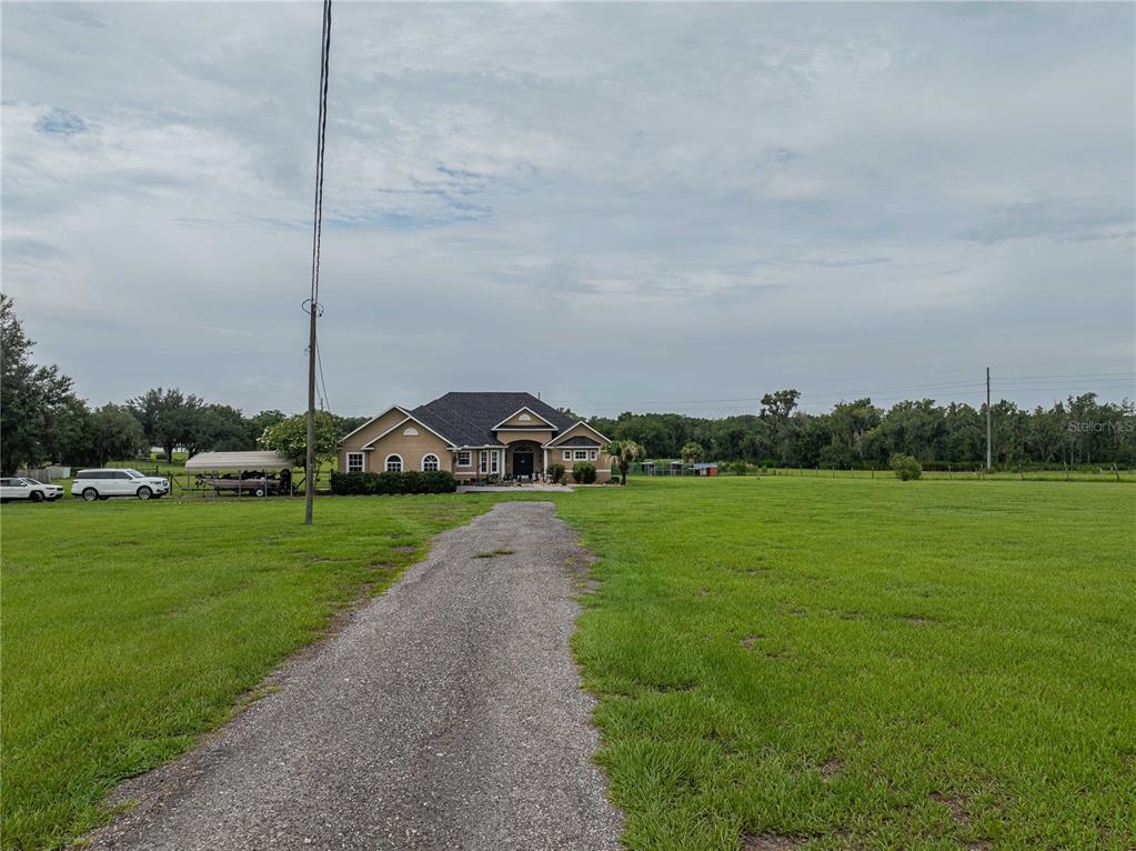 A gravel driveway leads to a tan house with a dark roof on a large lot — 4280 TURNER ROAD, MULBERRY, FL