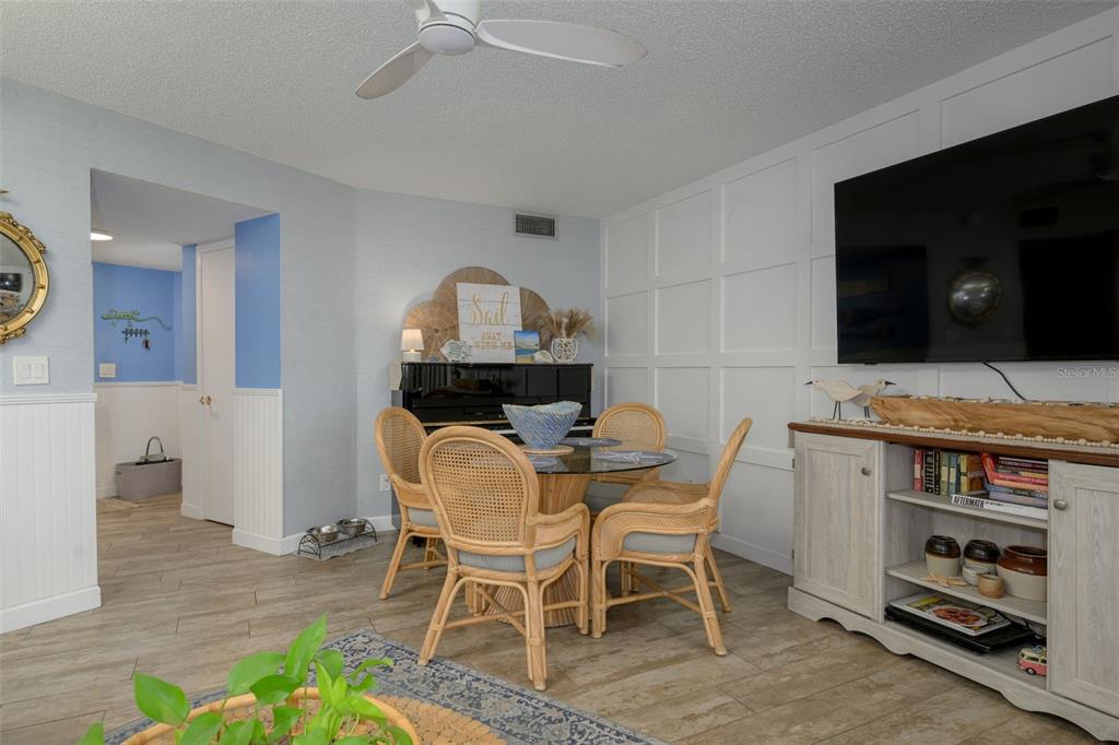A dining area features a glass-top table, wicker chairs, a piano, and a wall-mounted television — 3580 S OCEAN SHORE BOULEVARD UNIT 910, FLAGLER BEACH, FL