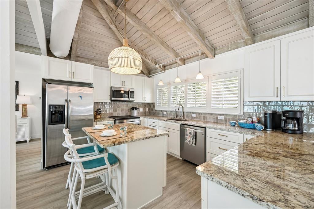 A kitchen features white cabinets, granite countertops, a center island with stools, and vaulted ceilings — 6570 MANASOTA KEY ROAD, ENGLEWOOD, FL