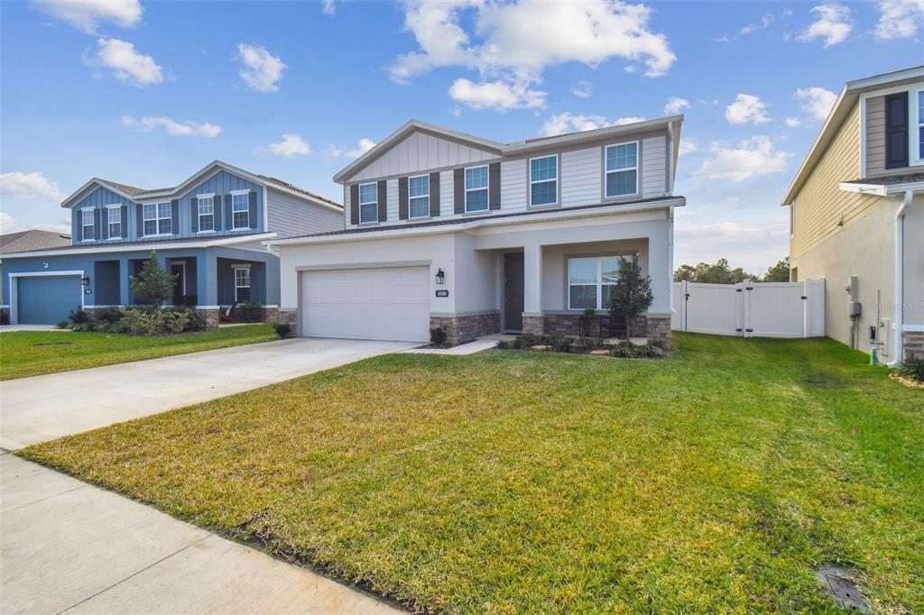 A two-story suburban house with a two-car garage, stone accents, and a white vinyl fence — 8308 GREENWAY AVENUE, WESLEY CHAPEL, FL