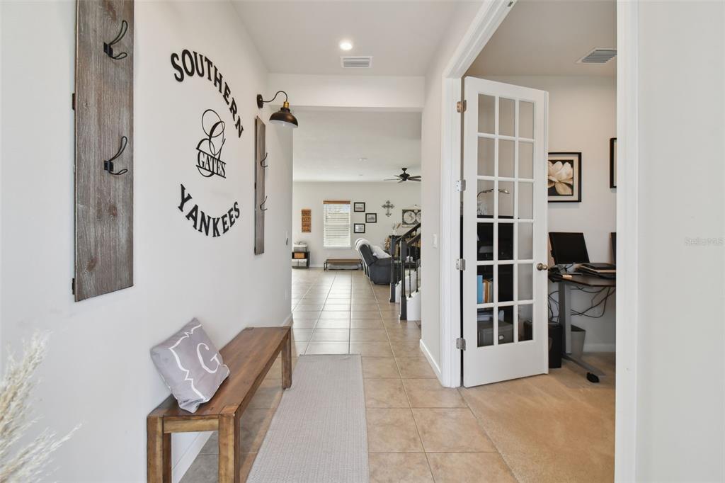 A hallway features a wooden bench, wall-mounted coat hooks, and a glass-paned office door — 8308 GREENWAY AVENUE, WESLEY CHAPEL, FL