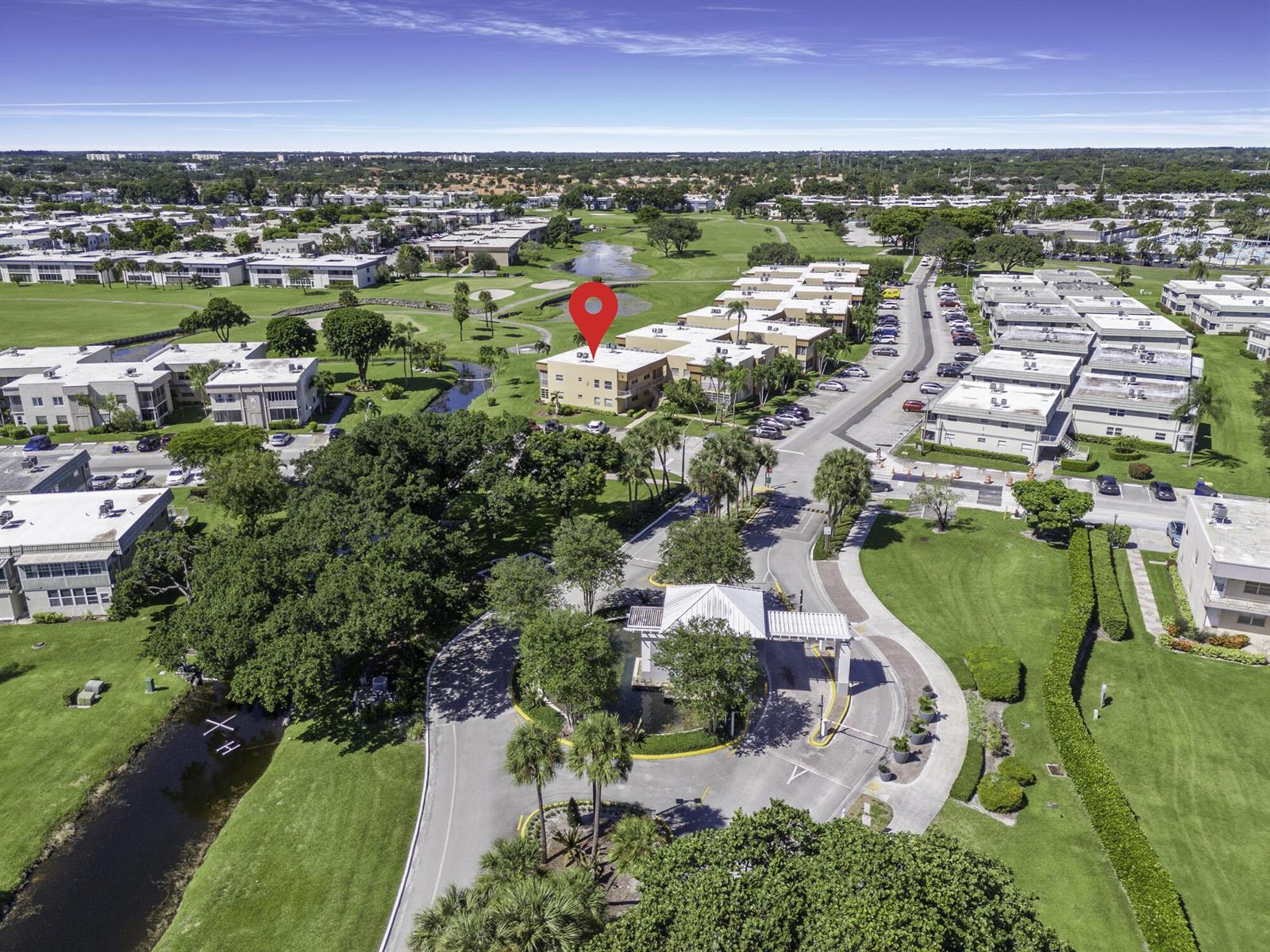 An aerial view shows a multi-story apartment building marked with a red pin near a pond — 480 Flanders J, Delray Beach FL 33484, DELRAY BEACH, FL