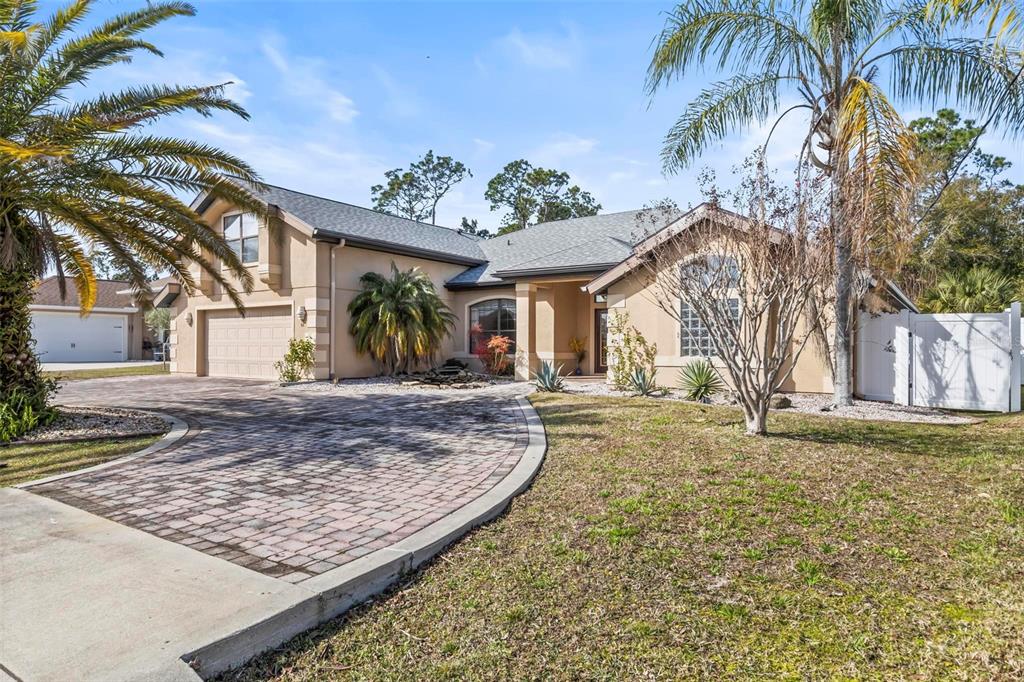 A tan single-story house with a paved driveway, palm trees, and a white fence — 88 COVINGTON LANE, PALM COAST, FL