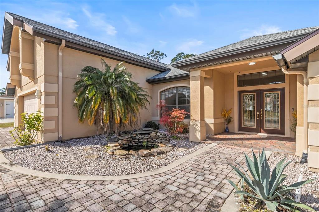 The exterior of a tan house features a stone fountain, a palm tree, and double doors — 88 COVINGTON LANE, PALM COAST, FL