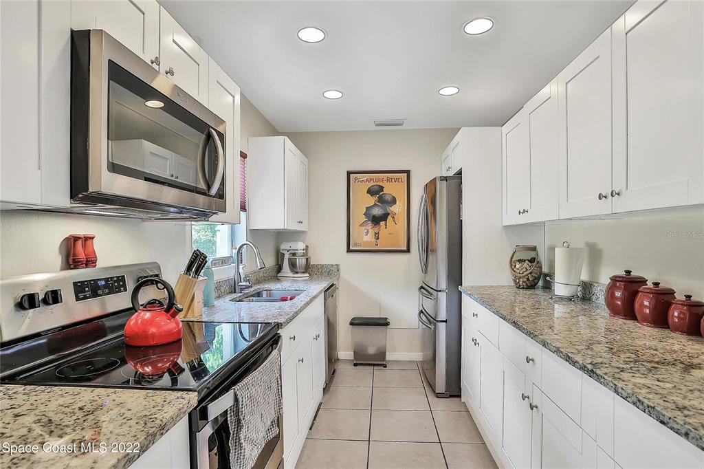 A galley kitchen features white cabinets, granite countertops, stainless steel appliances, and tile flooring — 1318 N FISKE BOULEVARD, COCOA, FL