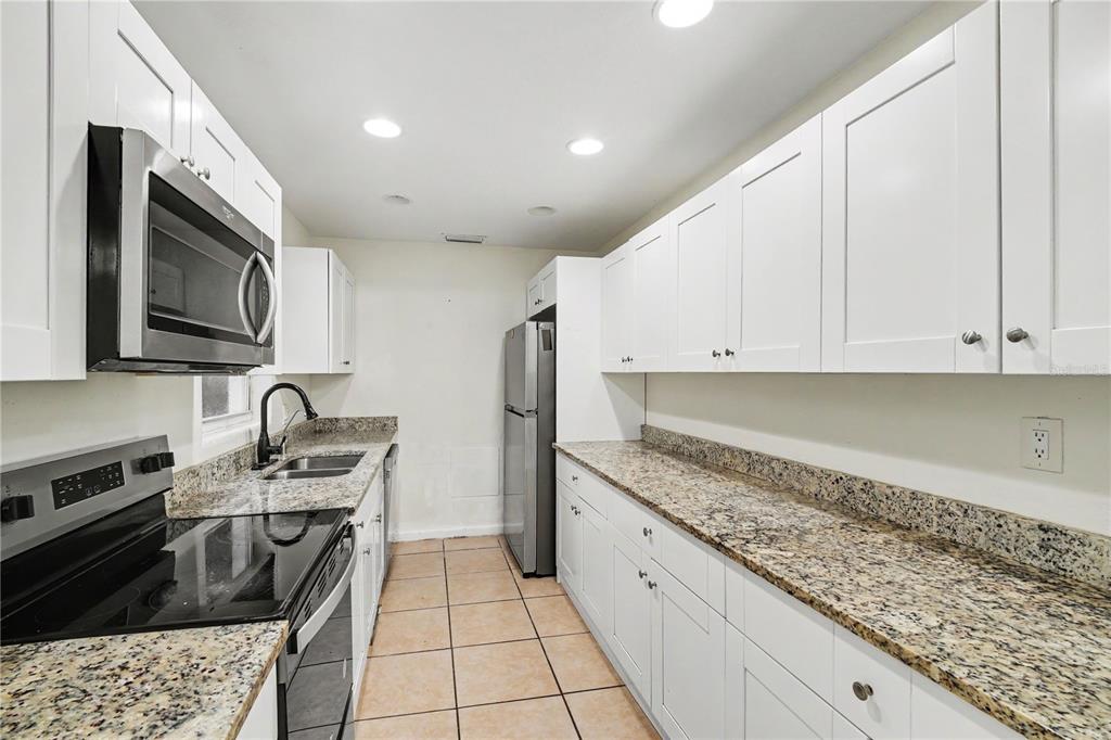 A galley kitchen features white cabinets, granite countertops, stainless steel appliances, and tiled flooring — 1318 N FISKE BOULEVARD, COCOA, FL