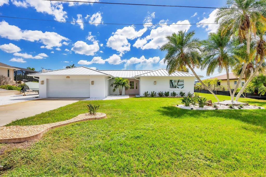 A white single-story house with a metal roof, two-car garage, and palm trees in front — 1915 PENNSYLVANIA AVENUE, ENGLEWOOD, FL