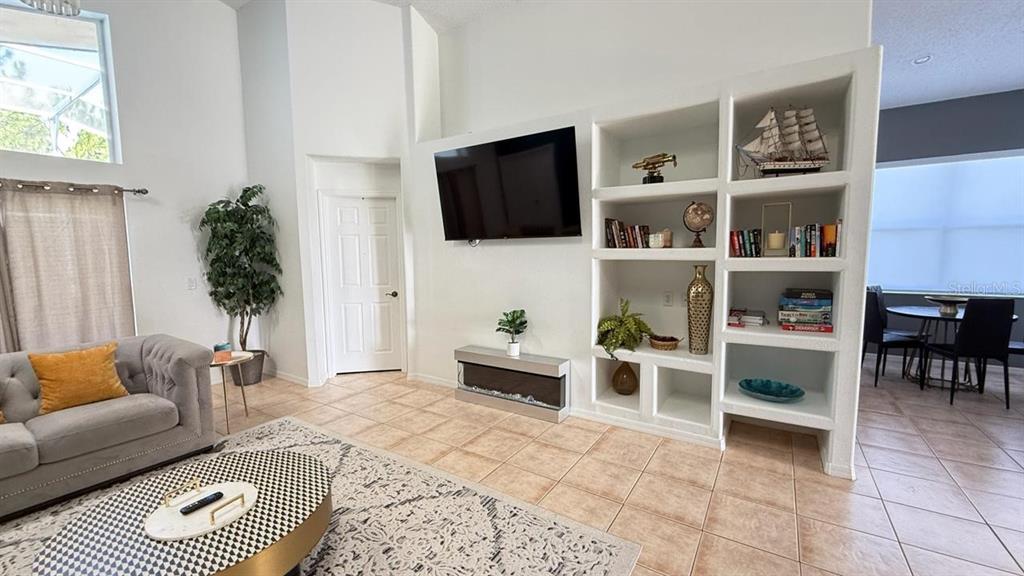A living room features a mounted television, built-in shelving, a fireplace, and tile flooring — 2659 AUTUMN CREEK CIRCLE, KISSIMMEE, FL