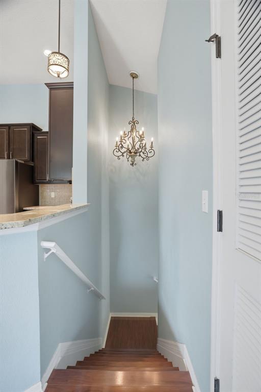 A staircase with wooden steps leads down past a chandelier and a kitchen counter — 7001 INTERBAY BOULEVARD UNIT 151, TAMPA, FL