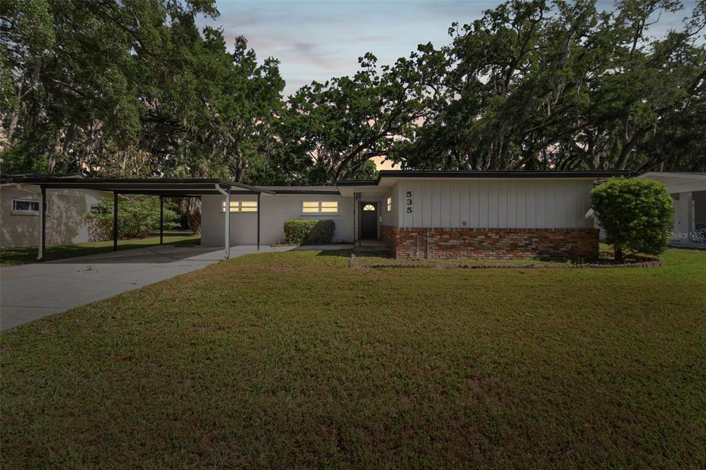 A single-story house with a carport, brick base, and light-colored siding under large trees — 535 W PALMEDEN DRIVE, LAKELAND, FL