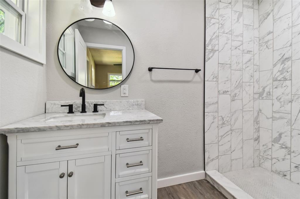 A bathroom features a white vanity with a marble countertop, a round mirror, and a shower — 535 W PALMEDEN DRIVE, LAKELAND, FL