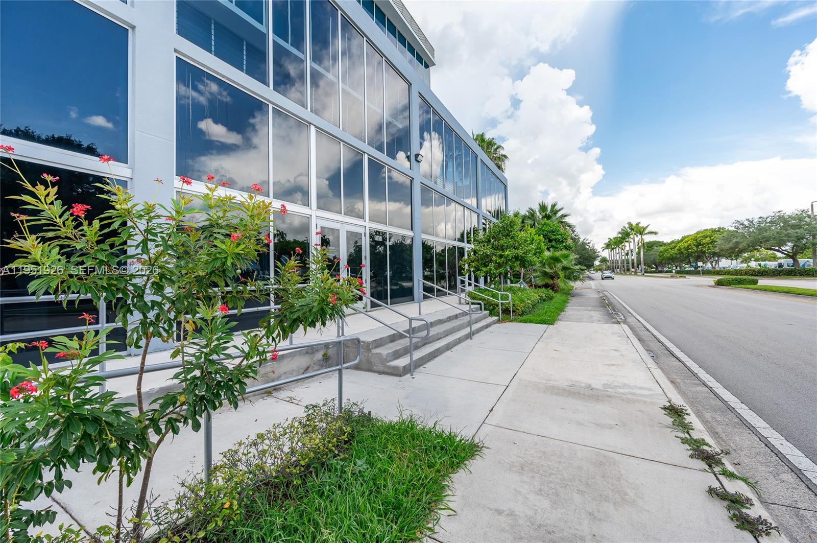 A modern office building exterior features large glass windows, concrete stairs, and a sidewalk — 10450 NW 33rd St # 501, Doral FL 33172, DORAL, FL