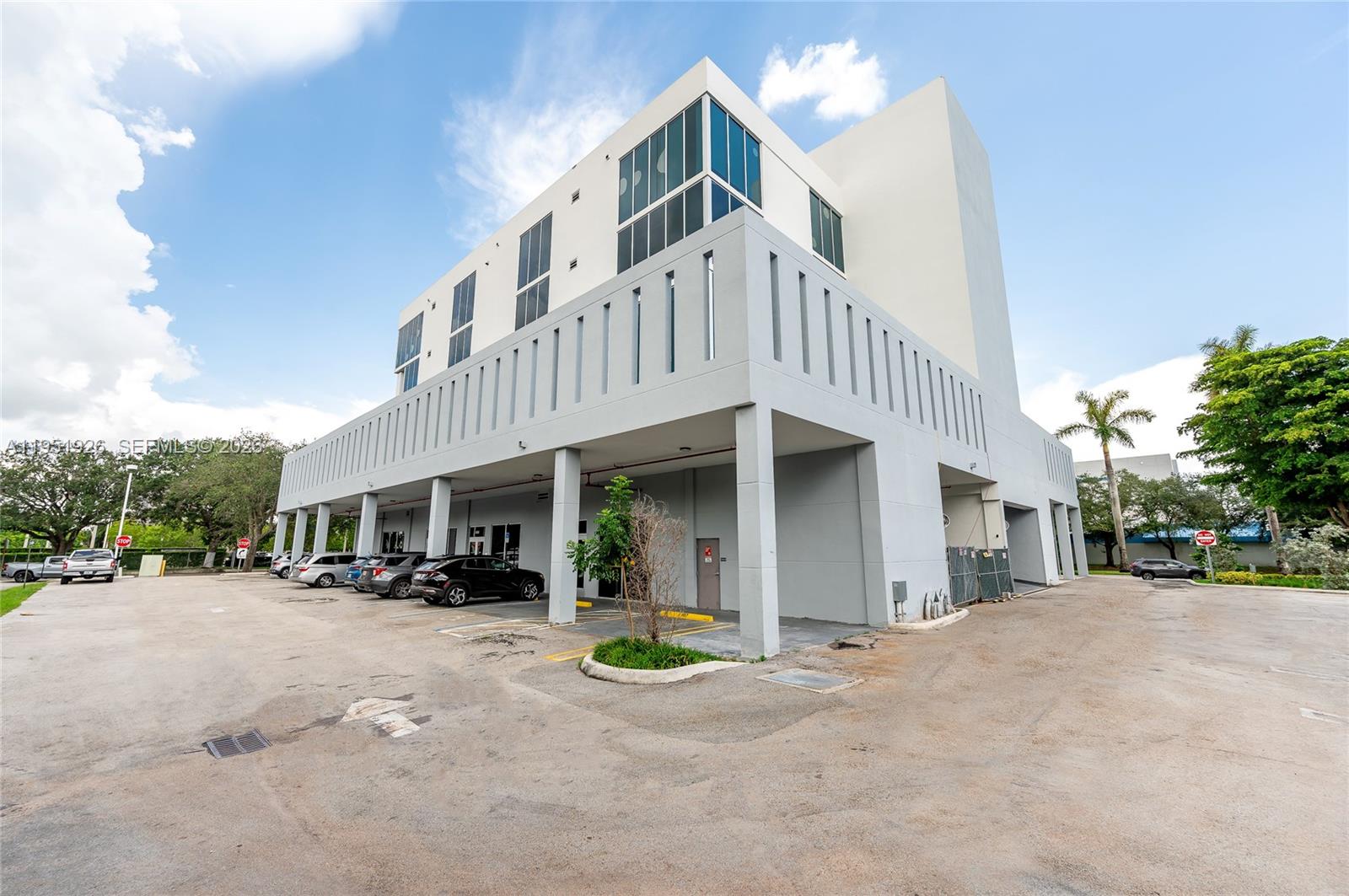 A modern multi-story commercial building with a covered parking area and a large paved lot — 10450 NW 33rd St # 501, Doral FL 33172, DORAL, FL