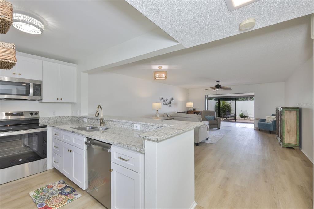 A kitchen with white cabinets and granite countertops overlooks an open-concept living area — 597 LAKESIDE DRIVE UNIT 597, BRADENTON, FL