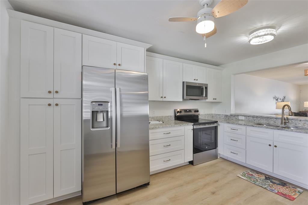 A kitchen with white cabinets, stainless steel appliances, granite countertops, and light wood-look flooring — 597 LAKESIDE DRIVE UNIT 597, BRADENTON, FL