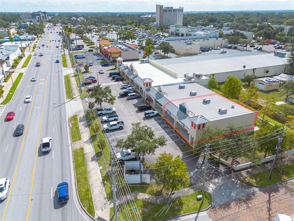 An aerial view shows a commercial strip mall with a parking lot beside a road — 1033 W BAY DRIVE, LARGO, FL