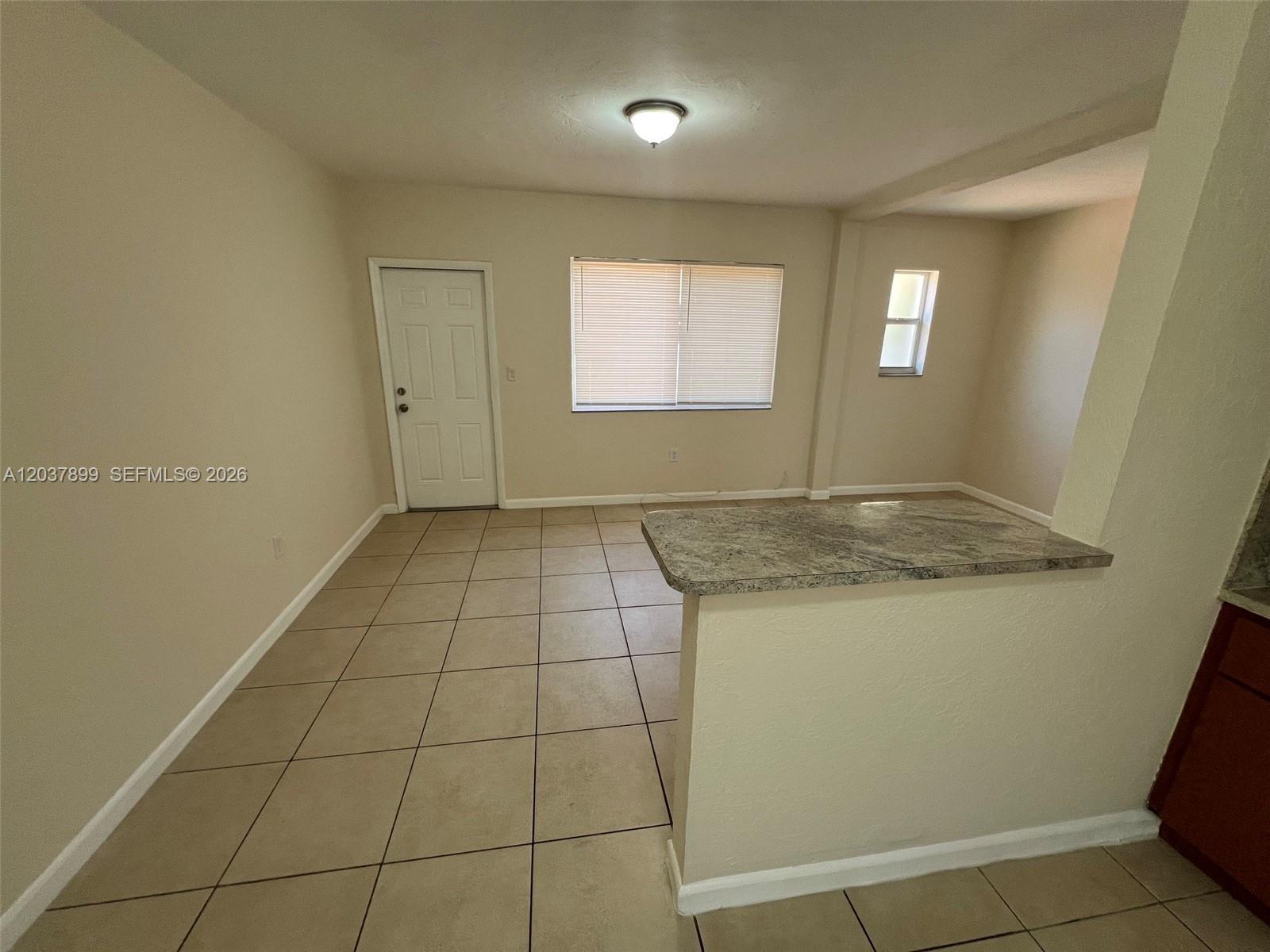 A room with beige walls, tiled flooring, a white door, and a granite-topped breakfast bar — 686 NE 85th St # 3B, Miami FL 33138, MIAMI, FL