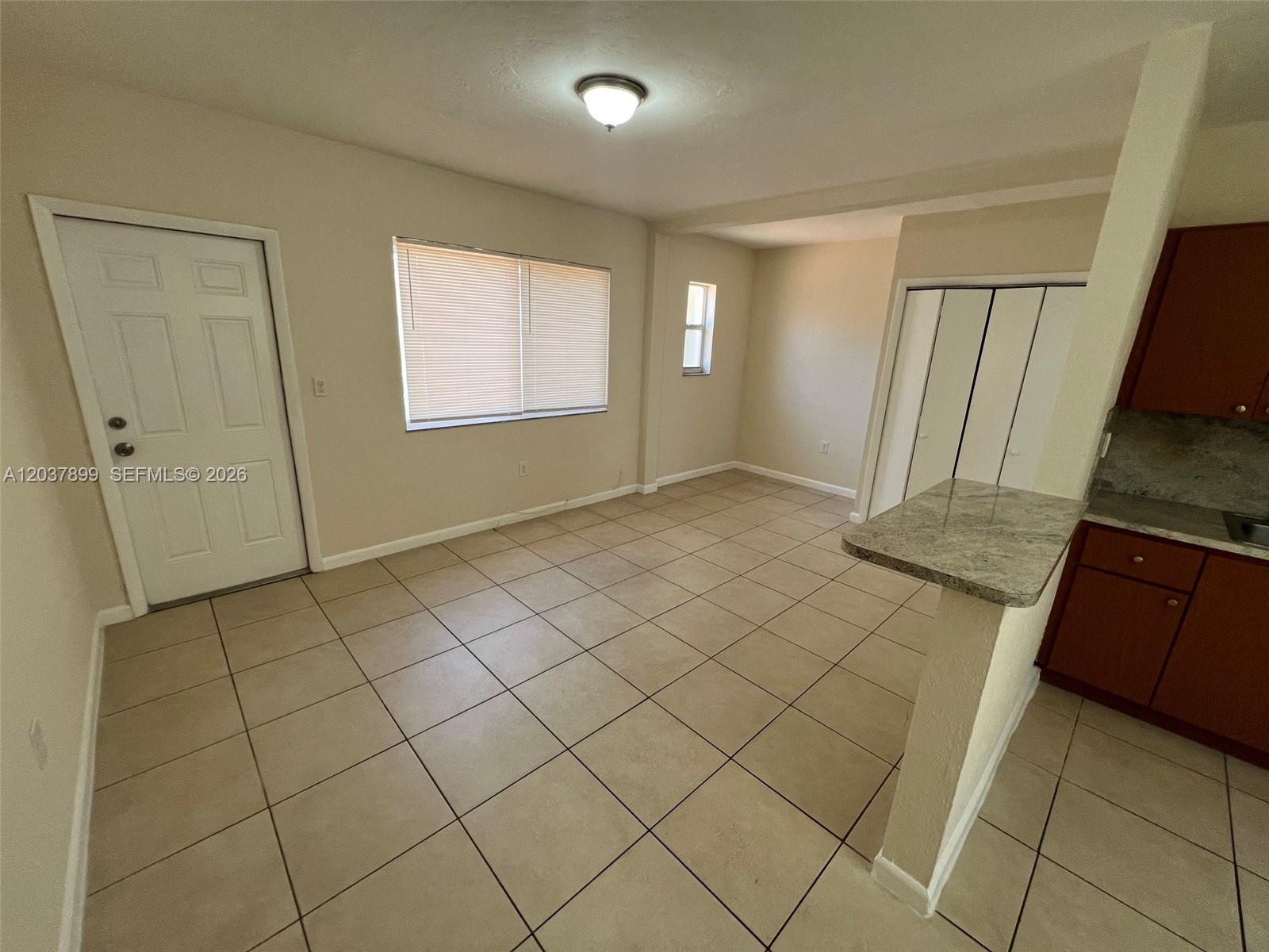 An open-concept dining area features beige tile flooring, a white door, and a kitchen pass-through — 686 NE 85th St # 3B, Miami FL 33138, MIAMI, FL