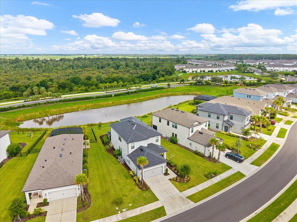 An aerial view shows suburban houses with dark roofs, green lawns, and a nearby pond — 9016 TEQUILA SUNRISE DRIVE, SARASOTA, FL