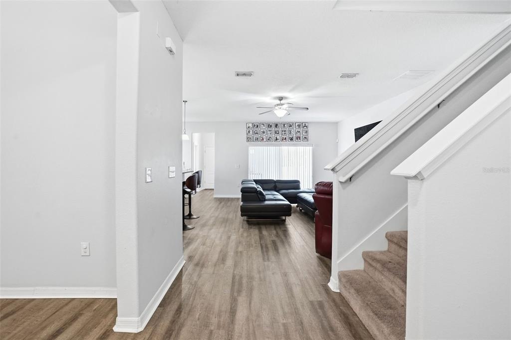 A view from a hallway looking into a living room with wood-look flooring and stairs — 2096 CORDAVILLE PLACE, APOPKA, FL
