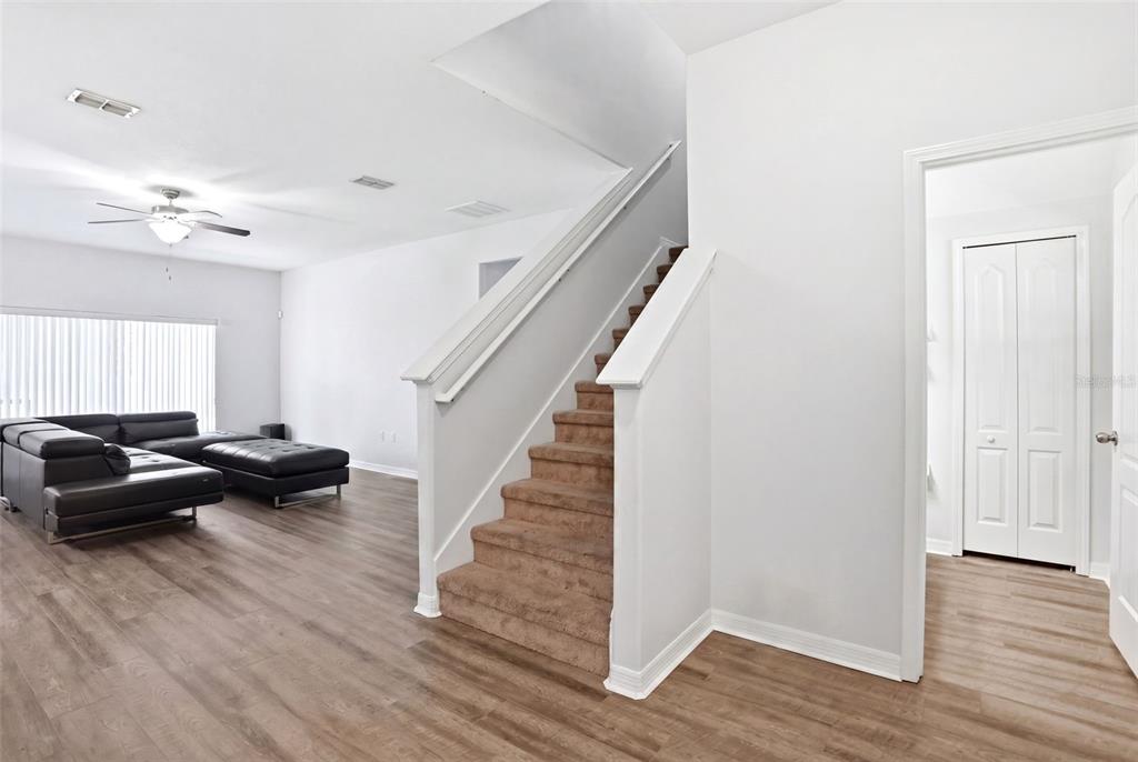 A living room with wood-look flooring, a sectional sofa, and carpeted stairs leading upward — 2096 CORDAVILLE PLACE, APOPKA, FL