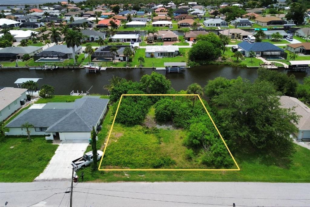 An aerial view shows a vacant, rectangular waterfront lot outlined in yellow next to a house — 5226 BOYLE TERRACE, PORT CHARLOTTE, FL